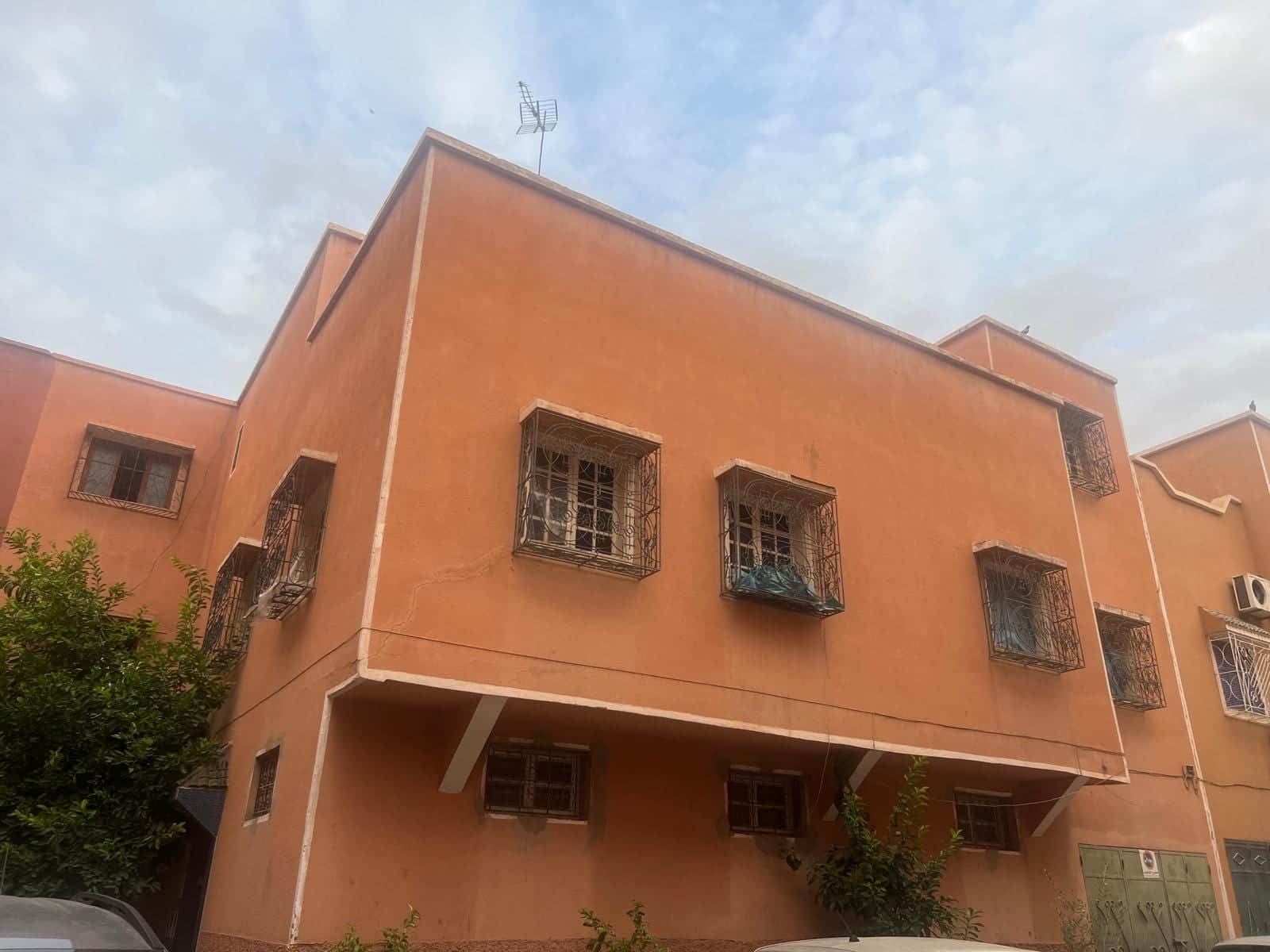 Façade ocre de la maison à étage, fenêtres à grilles en fer forgé sous un ciel nuageux